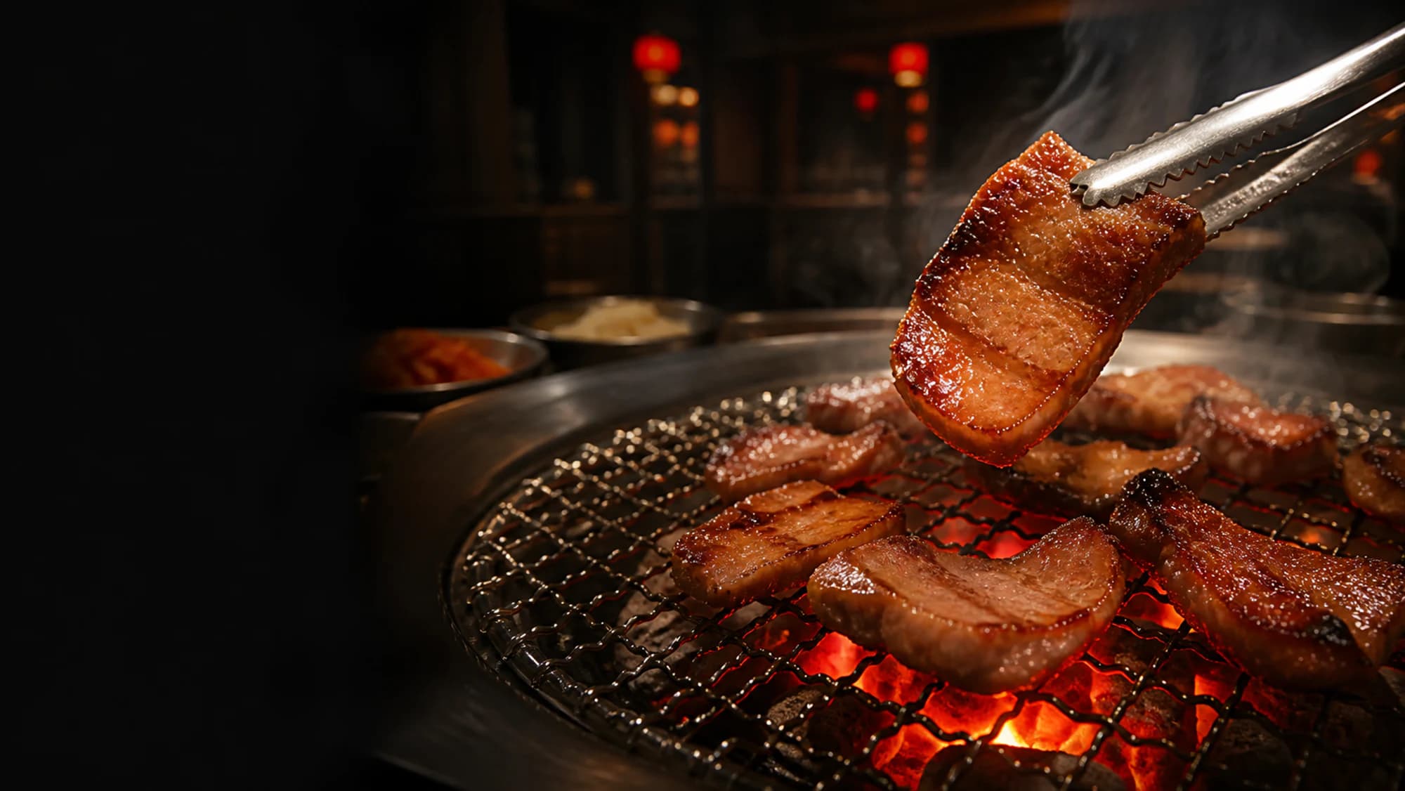 Caramelised pork belly being lifted with tongs above a glowing charcoal grill