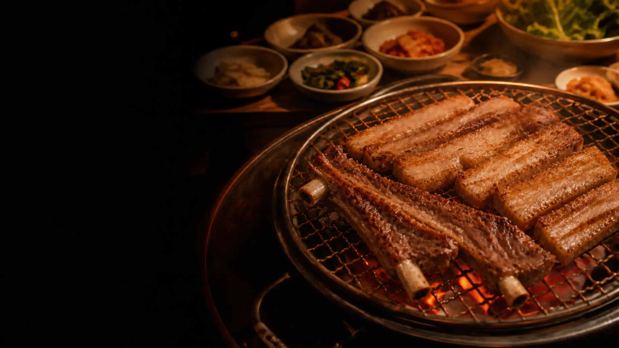 Caramelised pork ribs and thick pork belly grilling over glowing charcoal with Korean banchan